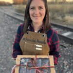 A woman smiling at the camera while holding a holiday box of assorted granola wrapped with red and green twine.